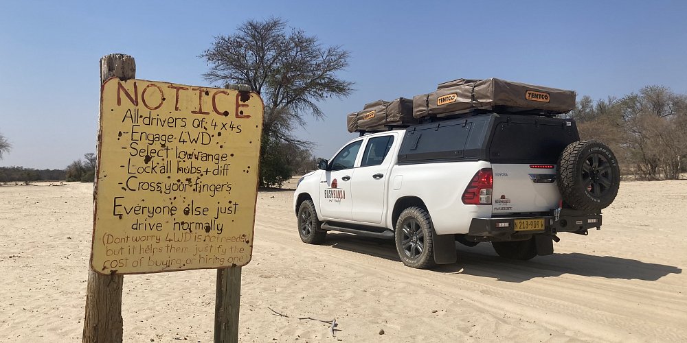 bushbundu-car-rental-windhoek-namibia-image-of-4x4-toyota-hilux-with-camping-equipment-in-the-desert-and-a-notice-table