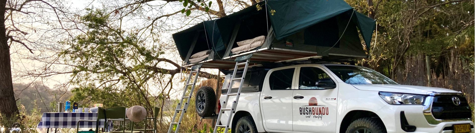 bushbundu-car-rental-windhoek-namibia-image-of-4x4-toyota-hilux-with-pitched-tents-on-the-rooftop-and-camping-set-about-us-page-cover-image