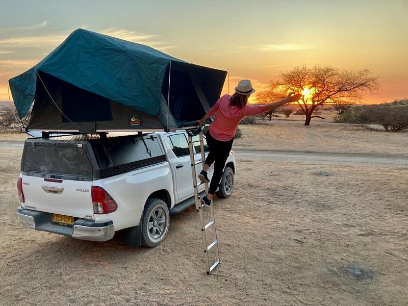 bushbundu-car-rental-windhoek-namibia-image-of-woman-climbing-to-her-tent-on-the-roof-of-toyota-hilux-waving-to-the-sunset-