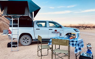 bushbundu-car-rental-windhoek-namibia-side-side-image-of-toyota-hilux-with-pitched-rooftop-tent-and-dining-table-spitzkoppe-camping-for-2