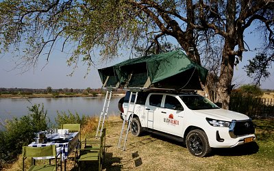 bushbundu-car-rental-windhoek-namibia-side-side-image-of-toyota-hilux-with-pitched-tent-on-the-roof-near-a-lake