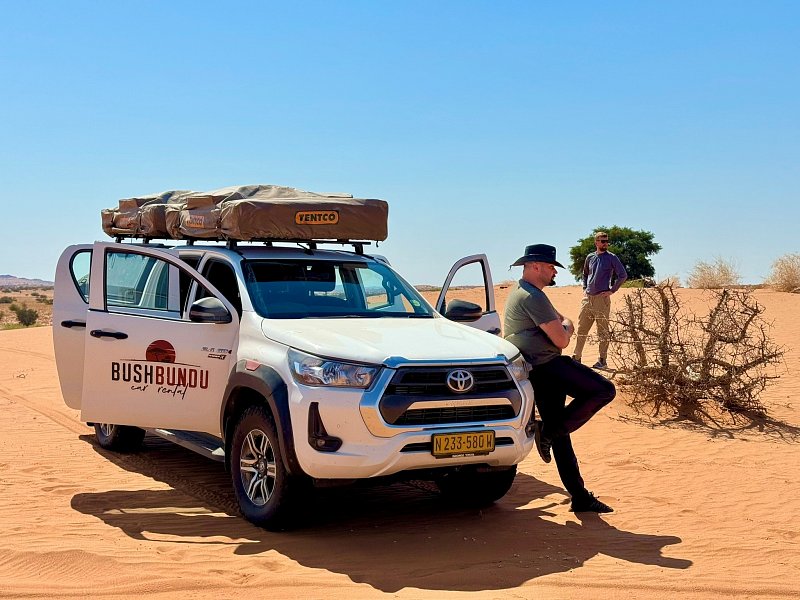 bushbundu-car-rental-windhoek-namibia-image-of-woman-climbing-to-her-tent-on-the-roof-of-toyota-hilux-waving-to-the-sunset-
